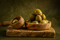 small bowl filled with green olives on a cutting board.